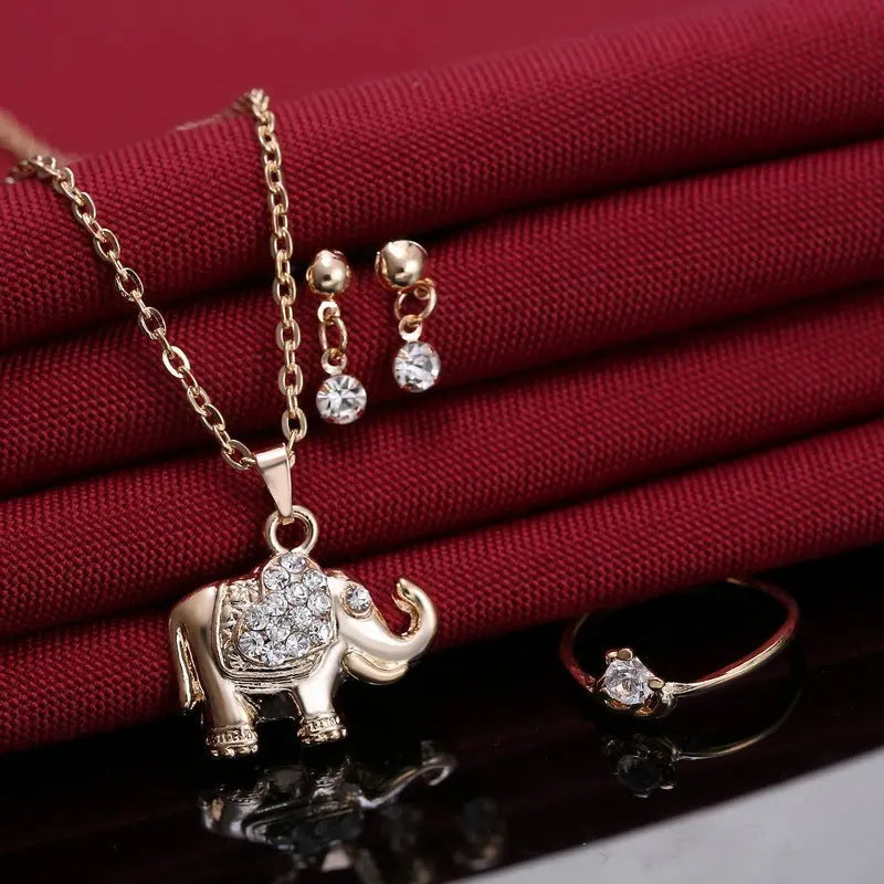 Parure éléphant doré avec strass présentée sur tissu rouge, incluant collier, bague et boucles. Animal Pendants, Necklaces, Rings, Jewelry, accessories.