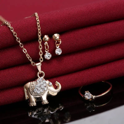 Parure éléphant doré avec strass présentée sur tissu rouge, incluant collier, bague et boucles. Animal Pendants, Necklaces, Rings, Jewelry, accessories.