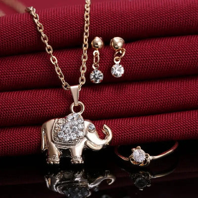 Collier éléphant doré avec strass et accessoires assortis sur fond rouge élégant. Animal Pendants, Necklaces, Rings, Jewelry, accessories.